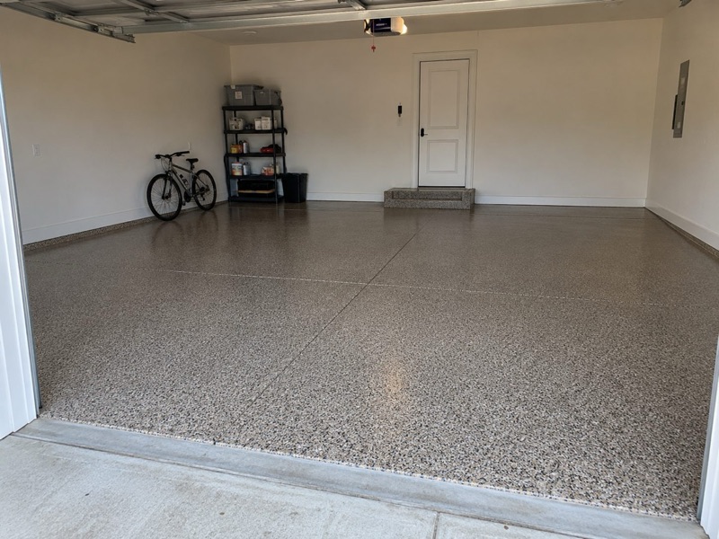 Finished tan and brown flake floor in an empty garage with a bicycle and a storage shelf